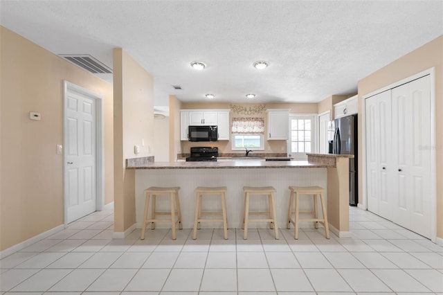 kitchen featuring stone countertops, black appliances, kitchen peninsula, and white cabinetry