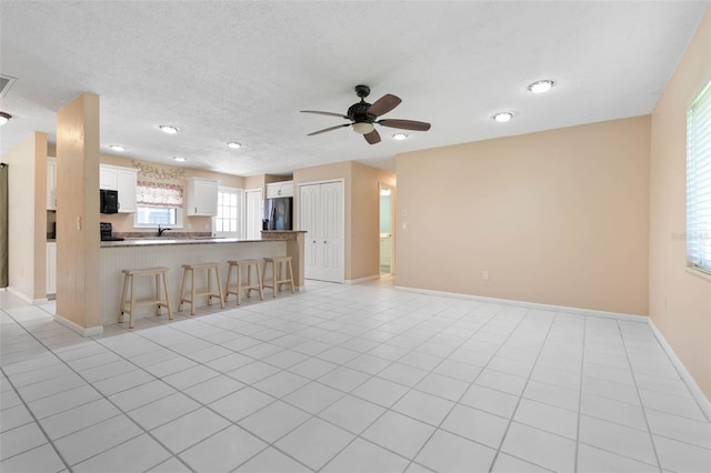 unfurnished living room with a textured ceiling, ceiling fan, and light tile patterned flooring