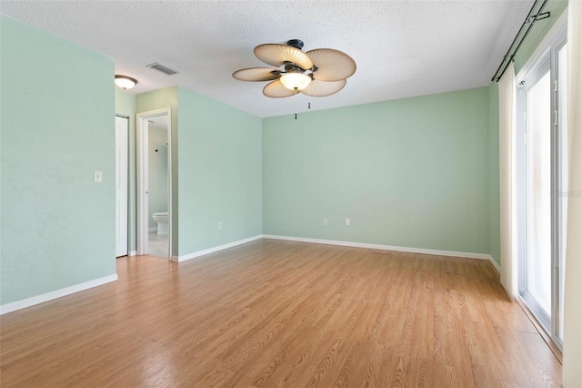 empty room featuring a textured ceiling, a healthy amount of sunlight, hardwood / wood-style floors, and ceiling fan