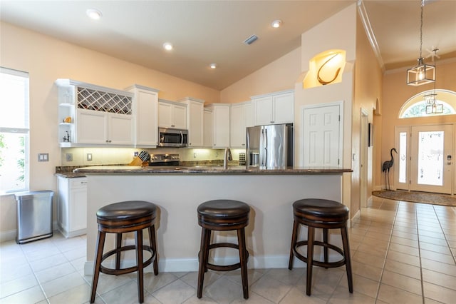 kitchen with appliances with stainless steel finishes, vaulted ceiling, light tile patterned floors, and white cabinets