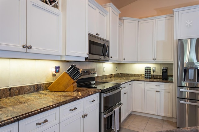 kitchen with white cabinets, stainless steel appliances, dark stone counters, light tile patterned flooring, and decorative backsplash