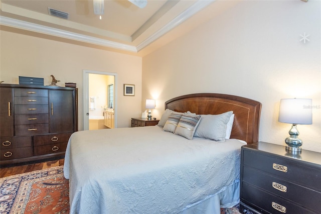 bedroom with dark hardwood / wood-style flooring, a tray ceiling, ceiling fan, connected bathroom, and ornamental molding