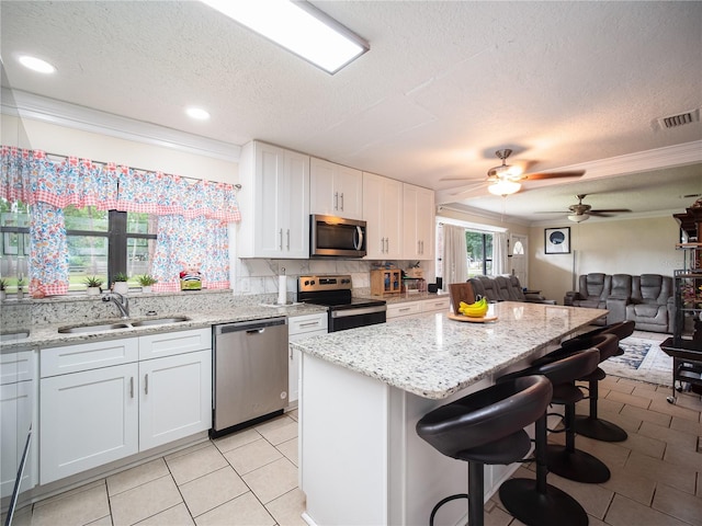 kitchen featuring sink, white cabinets, a kitchen bar, stainless steel appliances, and ceiling fan