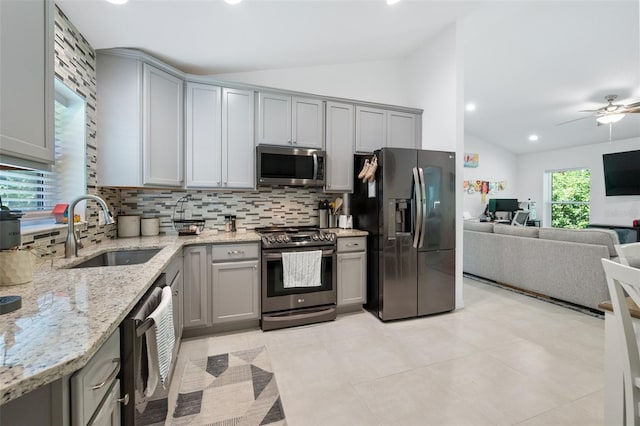 kitchen with lofted ceiling, gray cabinetry, a sink, appliances with stainless steel finishes, and decorative backsplash