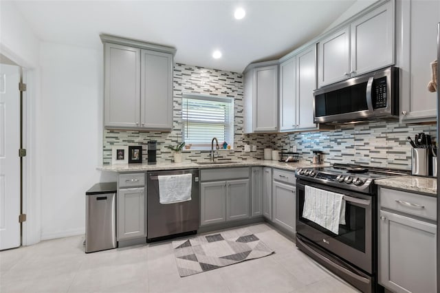 kitchen with backsplash, gray cabinets, stainless steel appliances, and a sink