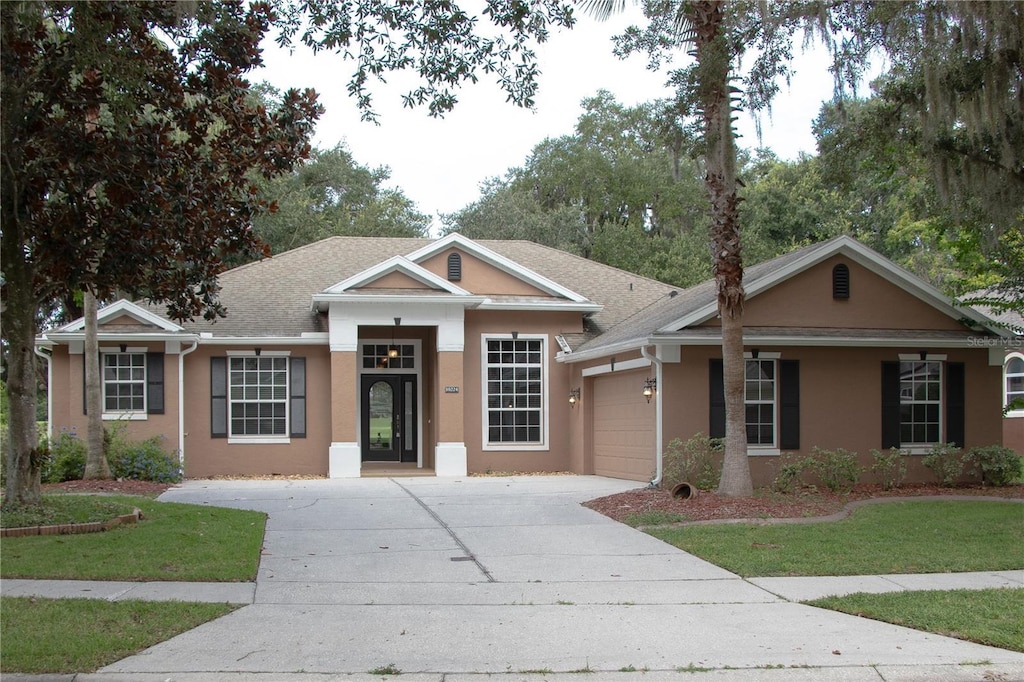 view of front of property with an attached garage, a shingled roof, concrete driveway, stucco siding, and a front lawn