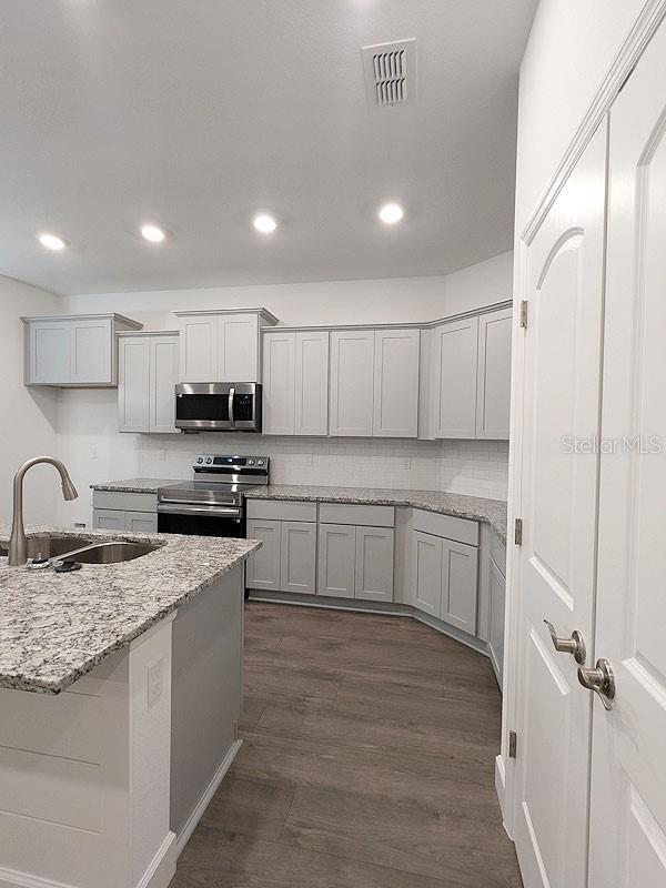 kitchen with tasteful backsplash, dark hardwood / wood-style floors, sink, light stone countertops, and appliances with stainless steel finishes