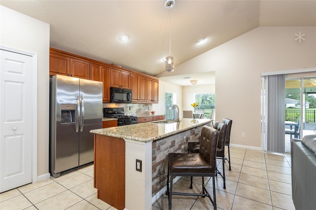 kitchen with an island with sink, black appliances, a healthy amount of sunlight, and light stone countertops