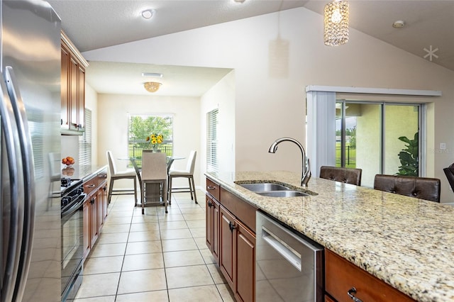 kitchen with vaulted ceiling, pendant lighting, appliances with stainless steel finishes, sink, and light stone counters