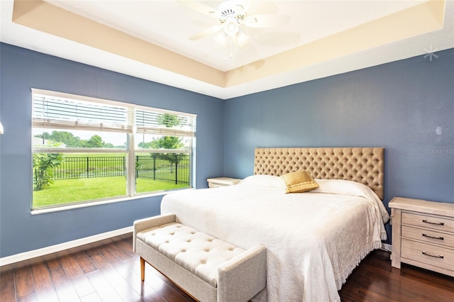 bedroom with ceiling fan, a tray ceiling, and dark hardwood / wood-style flooring