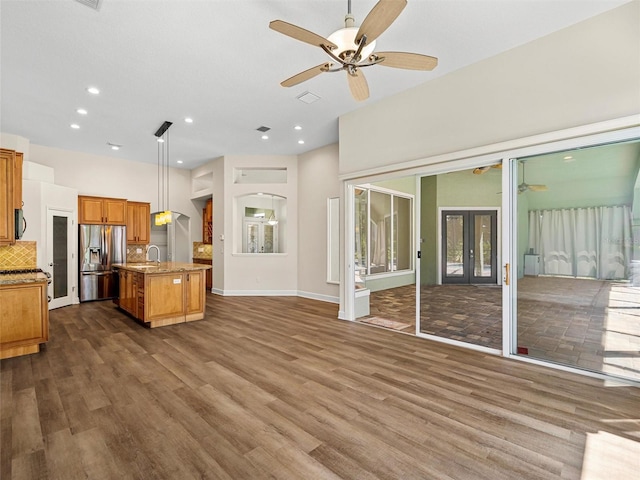 kitchen featuring dark hardwood / wood-style floors, a center island with sink, stainless steel fridge with ice dispenser, hanging light fixtures, and ceiling fan