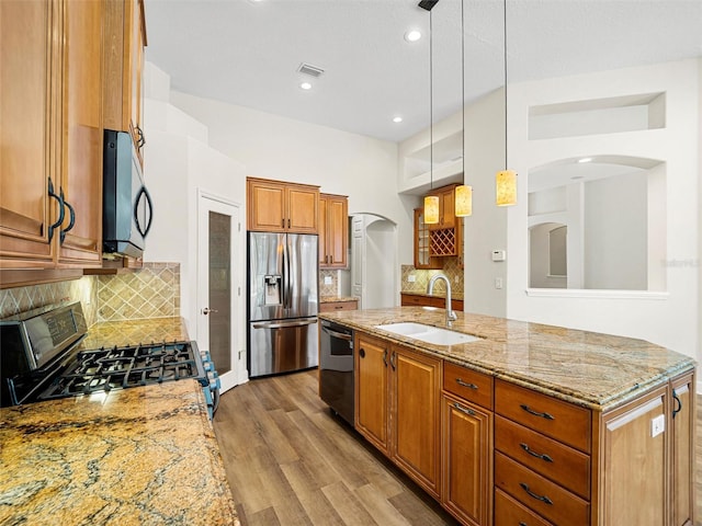 kitchen featuring decorative light fixtures, appliances with stainless steel finishes, tasteful backsplash, sink, and light wood-type flooring