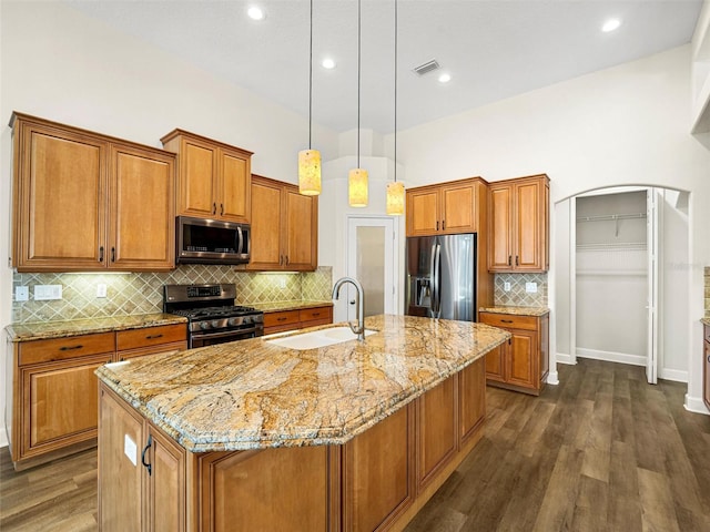 kitchen featuring a center island with sink, dark wood-type flooring, stainless steel appliances, sink, and light stone counters