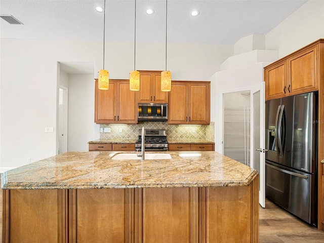 kitchen with light stone countertops, a center island with sink, light hardwood / wood-style floors, stainless steel appliances, and sink