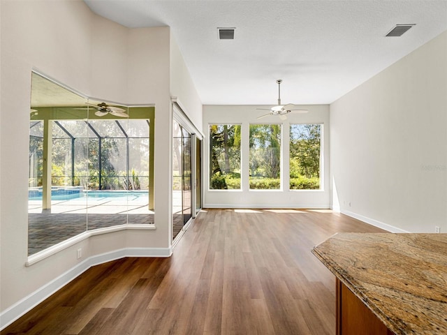 unfurnished dining area featuring wood-type flooring, plenty of natural light, a textured ceiling, and ceiling fan