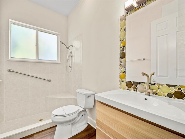 bathroom featuring vanity, wood-type flooring, backsplash, tiled shower, and toilet