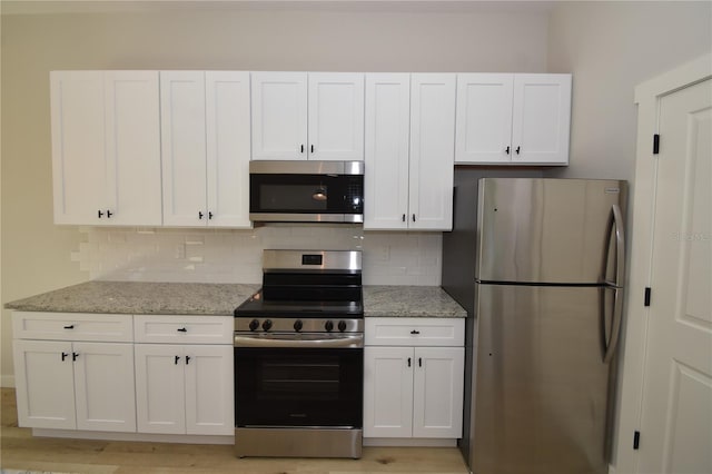 kitchen with light stone counters, appliances with stainless steel finishes, backsplash, and white cabinetry