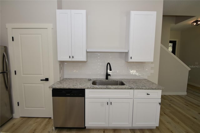 kitchen with stainless steel appliances, tasteful backsplash, white cabinetry, a sink, and light stone countertops