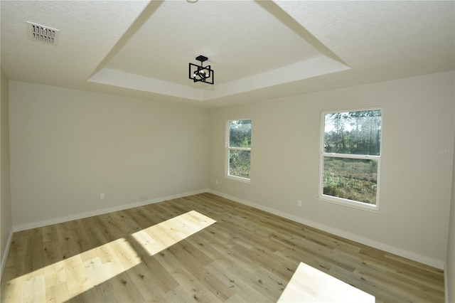 empty room featuring light wood-type flooring, baseboards, visible vents, and a raised ceiling