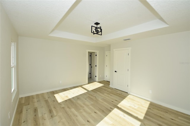 unfurnished room with light wood-type flooring, a raised ceiling, and a textured ceiling