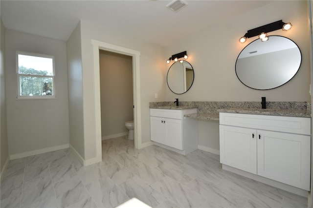 bathroom featuring toilet, two vanities, visible vents, baseboards, and marble finish floor