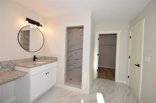 full bath with a walk in closet, marble finish floor, a marble finish shower, vanity, and baseboards