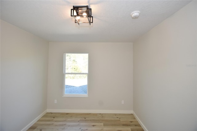 empty room featuring a textured ceiling, light wood-style flooring, and baseboards