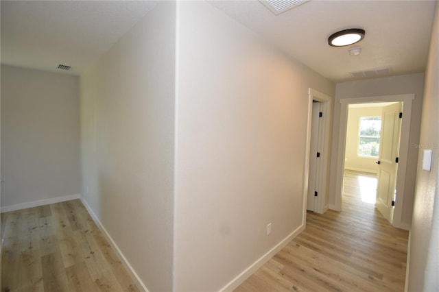 hallway featuring light wood-style flooring, visible vents, and baseboards