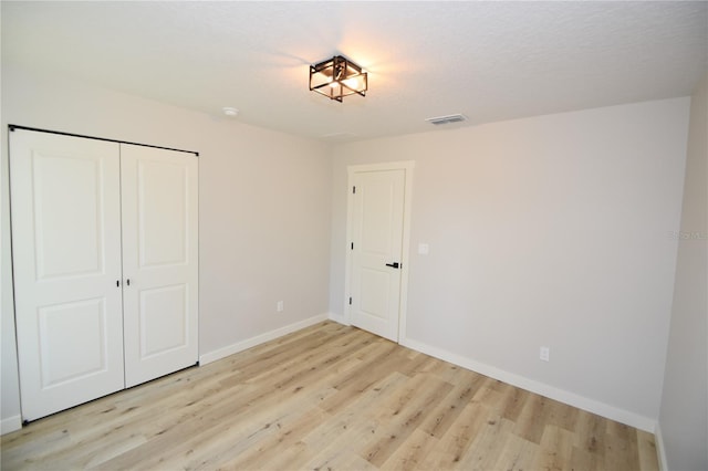 unfurnished bedroom with light wood finished floors, a closet, visible vents, and baseboards