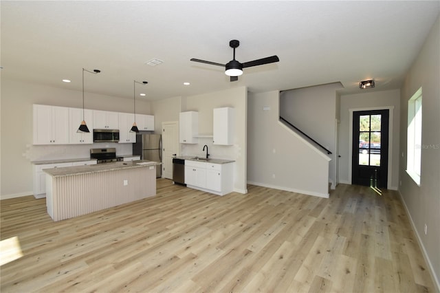 kitchen featuring a center island, decorative light fixtures, appliances with stainless steel finishes, white cabinets, and a sink