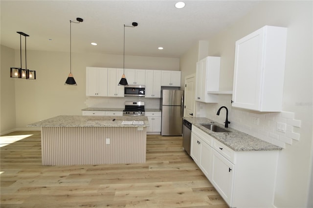 kitchen featuring stainless steel appliances, a sink, decorative light fixtures, and a center island