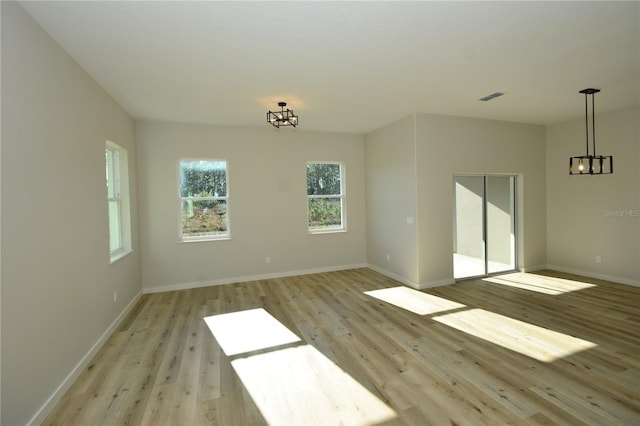 empty room featuring a chandelier, baseboards, visible vents, and light wood finished floors