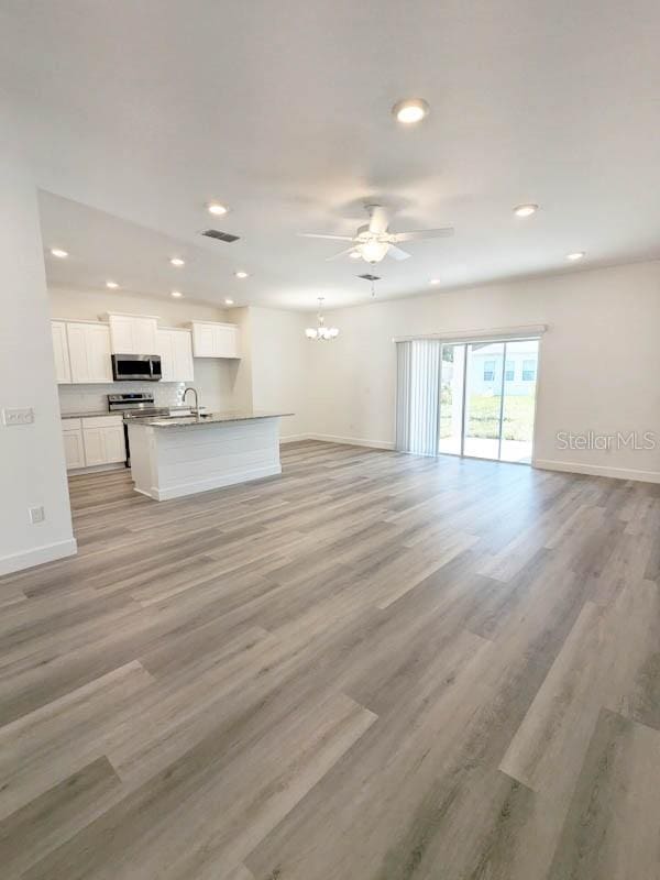 unfurnished living room featuring ceiling fan with notable chandelier, light wood-type flooring, and sink