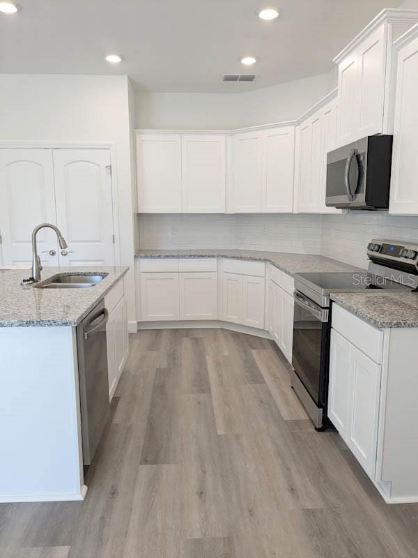 kitchen featuring sink, light stone countertops, appliances with stainless steel finishes, light hardwood / wood-style floors, and white cabinetry