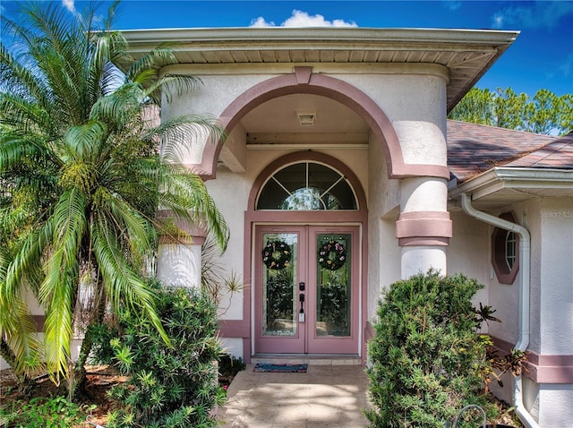 property entrance featuring french doors, roof with shingles, and stucco siding