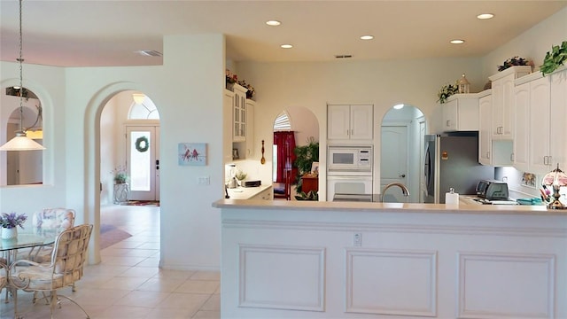 kitchen with white appliances, hanging light fixtures, kitchen peninsula, white cabinetry, and light tile patterned flooring