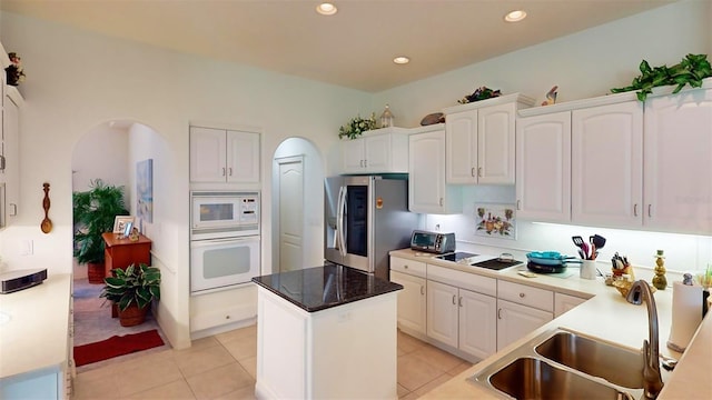 kitchen with white cabinets, light tile patterned floors, a center island, white appliances, and sink