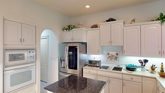 kitchen with dark stone countertops, white appliances, and white cabinetry