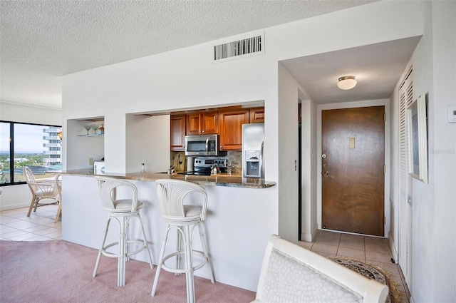 kitchen with a textured ceiling, light carpet, a breakfast bar, stainless steel appliances, and kitchen peninsula