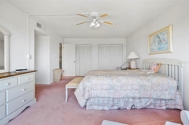 carpeted bedroom with a textured ceiling, two closets, and ceiling fan