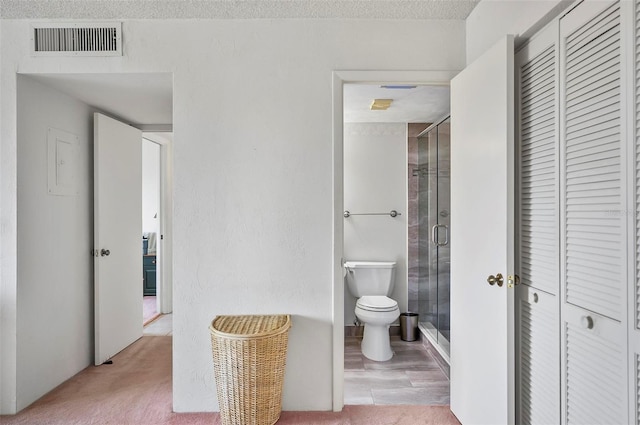 bathroom with a shower with door, toilet, and a textured ceiling