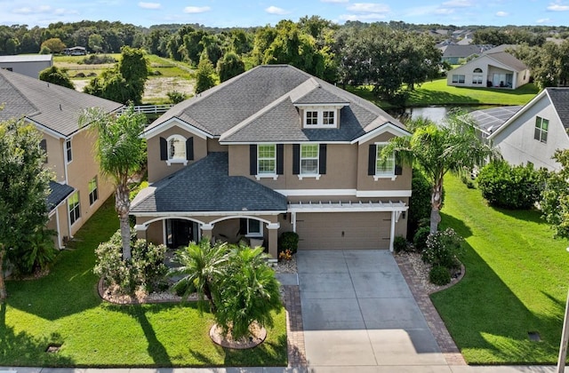 view of front facade with stucco siding, driveway, a shingled roof, and a front yard