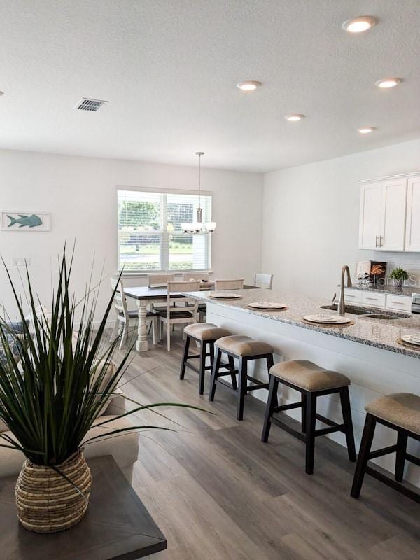 kitchen featuring white cabinets, hanging light fixtures, a textured ceiling, hardwood / wood-style flooring, and a kitchen breakfast bar