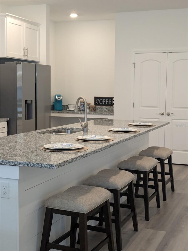 kitchen with a breakfast bar, light wood-type flooring, sink, white cabinetry, and stainless steel fridge