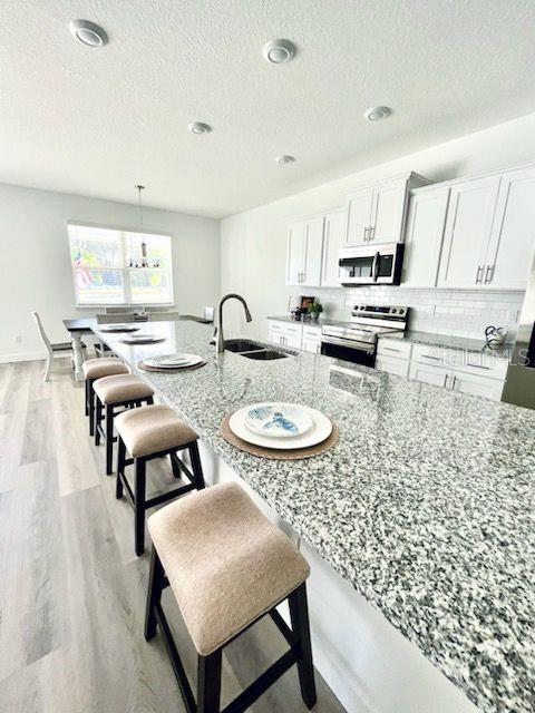 kitchen with white cabinets, light stone countertops, hanging light fixtures, stainless steel appliances, and light wood-type flooring