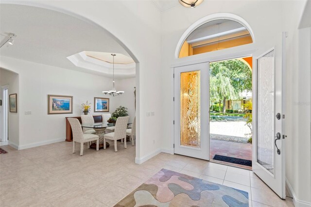 entrance foyer featuring a raised ceiling, an inviting chandelier, and light tile patterned floors