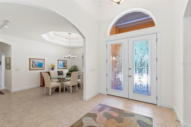 foyer with a tray ceiling, light tile patterned floors, a chandelier, and french doors