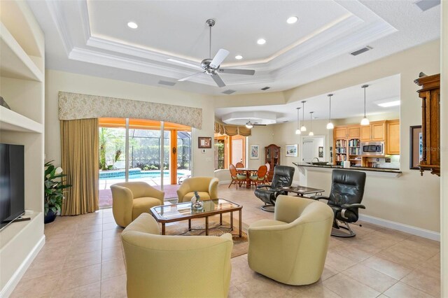 tiled living room featuring crown molding, ceiling fan, and a tray ceiling