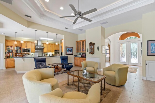 tiled living room with a tray ceiling, french doors, ornamental molding, and ceiling fan