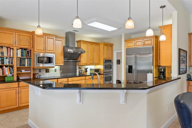 kitchen featuring built in appliances, hanging light fixtures, wall chimney exhaust hood, and kitchen peninsula